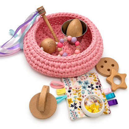 Cesto de los tesoros Blush Pink de trapillo rosa: detalle del cesto, el trapito y los accesorios sensoriales.
