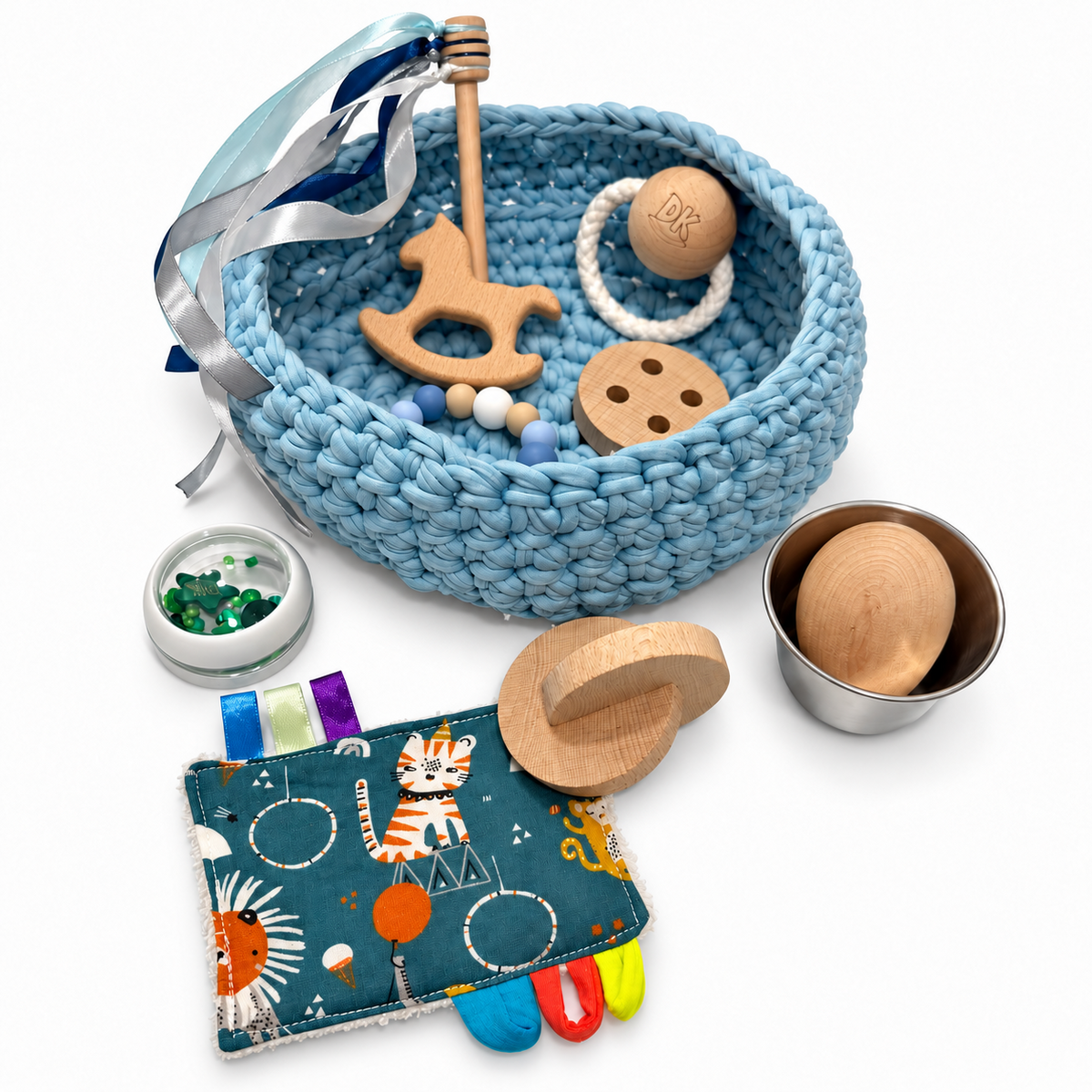 Cesto sensorial Dusty Blue con caballo de madera y accesorios alrededor: trapito estampado, discos, tarrito verde y flanera con huevo.