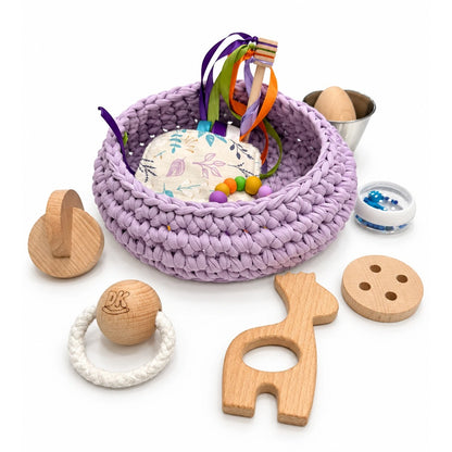 Cesto sensorial Lavender Mist con jirafa, discos entrelazados, botón y bola de madera alrededor.