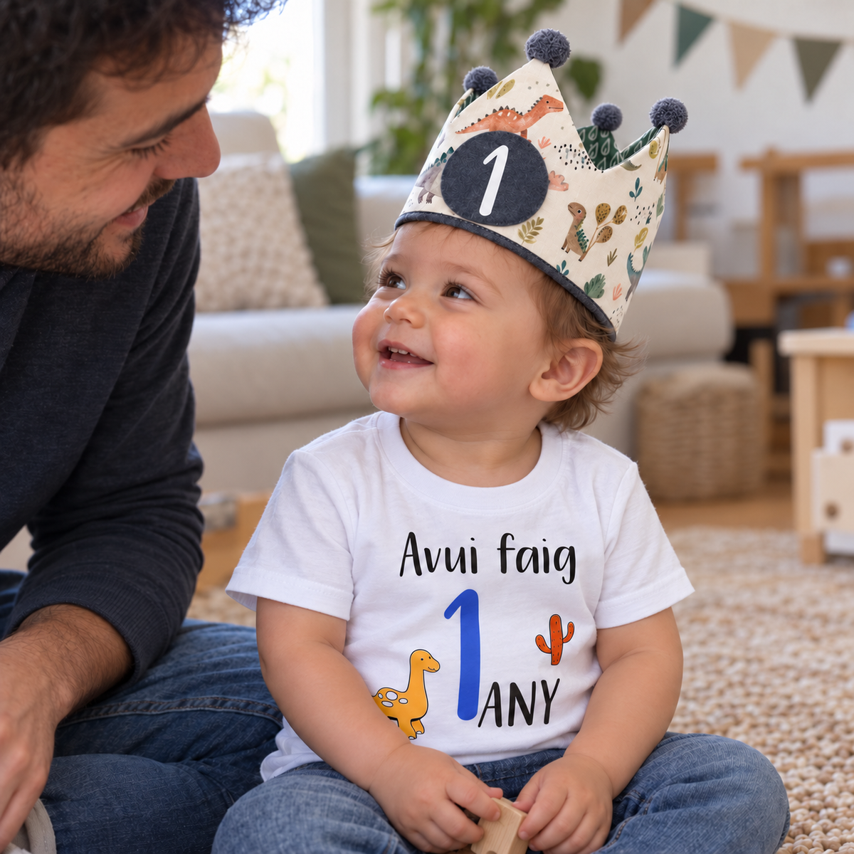 Bebé de un año con corona Dinos y camiseta de dinosaurio, junto a su padre